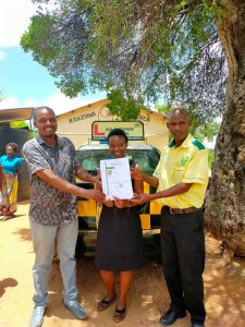 MoU signing — three leaders with document in front of AAKenya vehicle